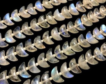 Puede incluir: Primer plano de hileras de cuentas en forma de media luna. Las cuentas translúcidas muestran un brillo iridiscente con tonos azules y blancos. Están ensartadas, creando un patrón repetitivo sobre un fondo negro. Ideal para joyería.
