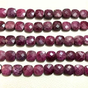 May include: A strand of pink ruby gemstone beads, each bead is faceted and has a square shape.