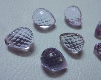 May include: A collection of six faceted amethyst teardrop shaped gemstones. The gemstones are a pale lavender color and have a smooth, polished finish.