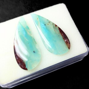 May include: Two teardrop-shaped cabochons of blue opal with brown inclusions. The stones are set in a white foam display box.