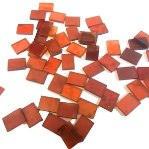May include: A collection of small, rectangular, translucent, amber-colored glass tiles. The tiles are scattered on a white surface.