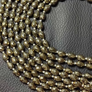 May include: A strand of faceted pyrite beads in a teardrop shape. The beads are a dark gold colour and have a metallic sheen.