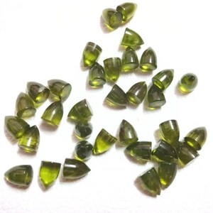 Puede incluir: Una colecci&oacute;n de cabujones de piedras preciosas verdes, cada uno con una punta puntiaguda, esparcidos sobre una superficie blanca.