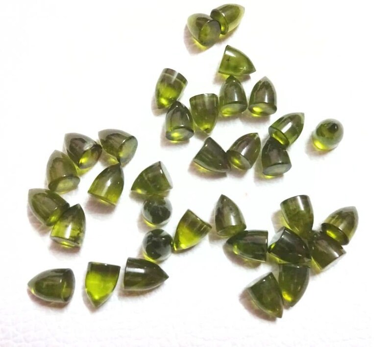 Puede incluir: Una colecci&oacute;n de cabujones de piedras preciosas verdes, cada uno con una punta puntiaguda, esparcidos sobre una superficie blanca.