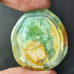 Könnte beinhalten: Ein grüner und brauner Cabochon-Edelstein mit einem geschichteten Muster. Der Edelstein ist rund und hat eine glatte, polierte Oberfläche.