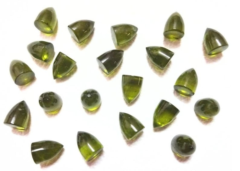 Puede incluir: Una colecci&oacute;n de 20 cabujones de piedras preciosas verdes de diversas formas y tama&ntilde;os. Los cabujones est&aacute;n todos cortados en forma puntiaguda, algunos son m&aacute;s redondeados que otros. Las piedras son de color verde oscuro, algunas tienen un ligero tono amarillo.