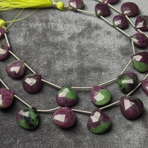 Puede incluir: Hilos de cuentas de piedras preciosas. Las cuentas son una mezcla de rojo intenso y verde, con un corte facetado. Los hilos están ensartados en un alambre plateado y están acentuados con borlas amarillas brillantes.