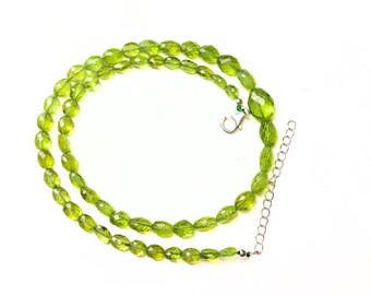 May include: A green peridot gemstone necklace with a silver clasp and extender chain.