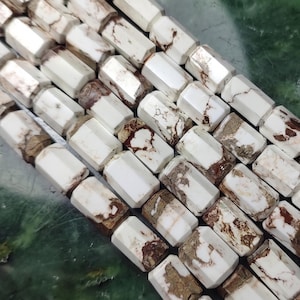 May include: A collection of white and brown marbled stone beads arranged in parallel rows. Each bead features a faceted hexagonal shape with a smooth, polished finish, displaying natural veining patterns in shades of earthy brown against a white base.
