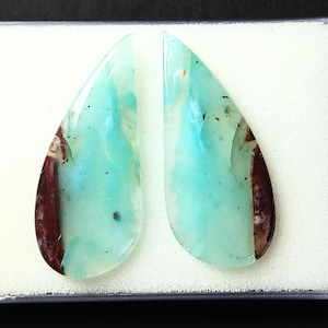 May include: A pair of teardrop-shaped cabochon gemstones with a blue-green color and brown inclusions. The stones are displayed in a white box.