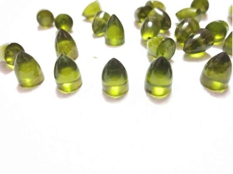 Puede incluir: Una colecci&oacute;n de cabochones de piedras preciosas verdes, cada uno con una parte superior puntiaguda y una base redondeada. Las piedras son transl&uacute;cidas y tienen un ligero brillo.