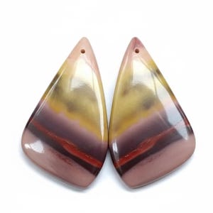 May include: Two polished, teardrop-shaped gemstones with a hole at the top. The stones feature layers of colour, including shades of pink, yellow, burgundy, and red. The gemstones are smooth and reflective, ideal for jewellery making.