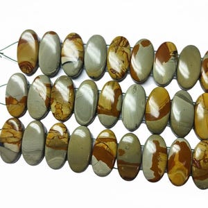 May include: Three strands of oval beads in shades of brown, tan, and grey. Each bead has a unique pattern. White tassels are attached to the ends of each strand. The beads are strung together with green thread.