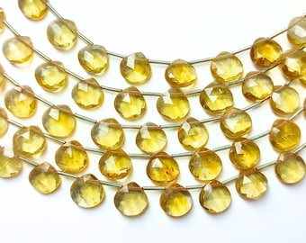 May include: Strands of faceted, yellow gemstone beads. The beads are strung on silver-colored wire and arranged in multiple rows. Orange tassels are visible on the left side of the image. The beads have a pear-like shape and a translucent quality.