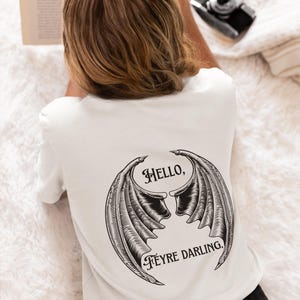 May include: White t-shirt with a black graphic of a pair of wings with the text "Hello, Feyre Darling."