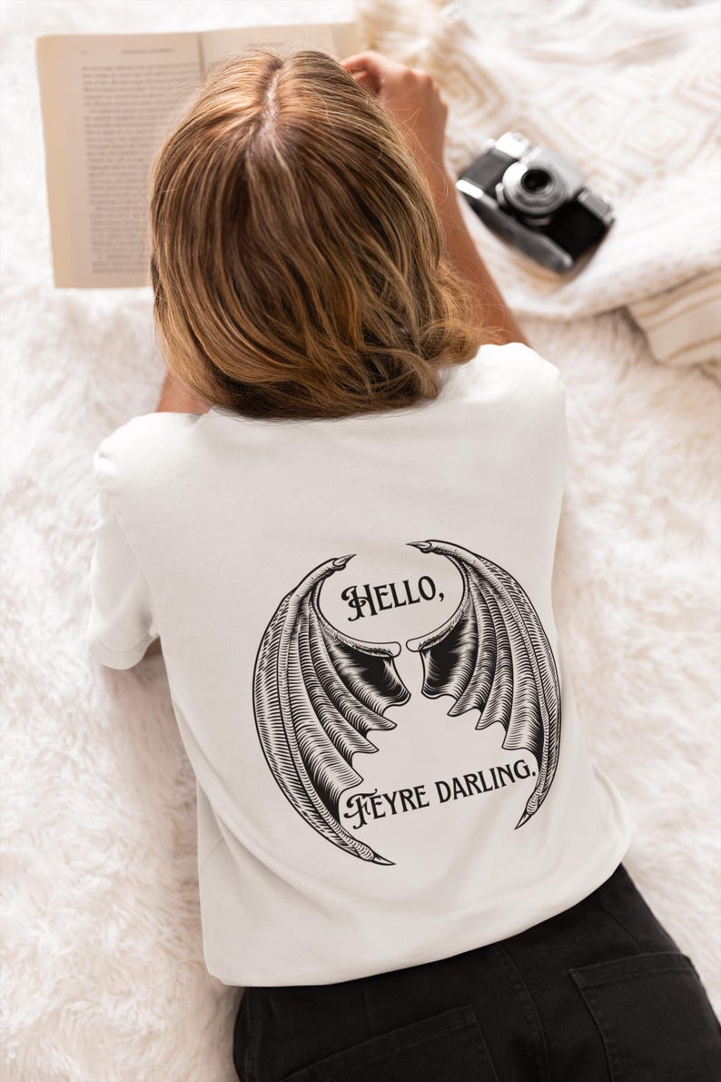 May include: White t-shirt with a black graphic of a pair of wings with the text "Hello, Feyre Darling."