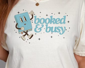 May include: A white t-shirt with a blue cartoon book character and the text "booked & busy".