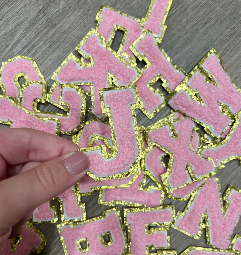 May include: A pile of pink felt letters with gold glitter trim. The letters are in various sizes and are arranged in a random order.