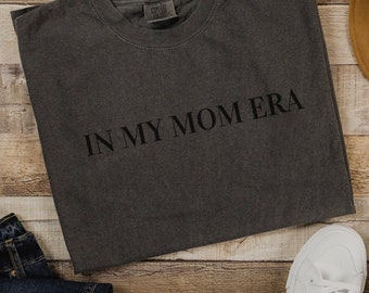 May include: A dark gray t-shirt with the text "IN MY MOM ERA" printed in black on the front.
