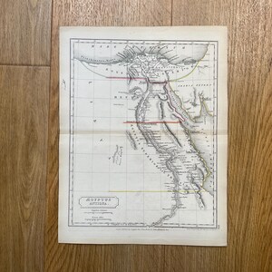 Op de afbeelding: Een antieke kaart van Egypte, met gedetailleerde geografische elementen. De kaart is gedrukt op verouderd papier, met een rasteroverlay en tekstlabels. De kaart bevat de Nijl en de omliggende gebieden, met rode en gele lijnen. De kaart is gevouwen.