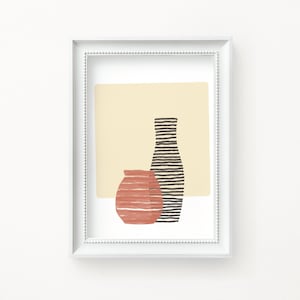 May include: A framed art print featuring an abstract design. The artwork showcases two stylized vases in shades of terracotta and black, set against a pale yellow backdrop. The frame is white with a beaded border.