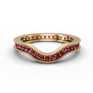 May include: A gold wedding band with a curved, wave-like design. The band is set with a row of small, red gemstones.