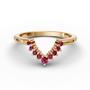 Op de afbeelding: Een gouden ring met een V-vormige rij kleine rode edelstenen.