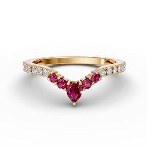 Könnte beinhalten: Ein goldener Ring mit einem birnenförmigen Rubin-Edelstein und kleineren Rubin- und Diamant-Akzenten. Der Ring hat ein V-förmiges Band.