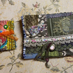 Può includere: Una piccola pochette rettangolare in tessuto con un nastro arancione brillante e una pochette rettangolare più grande con patchwork, ricami, bordi in pizzo e bottoni decorativi. Entrambi gli articoli sono realizzati con vari ritagli di tessuto.