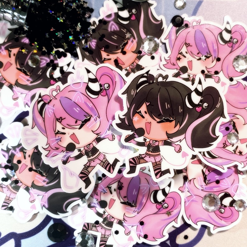 May include: A set of five colorful cartoon character stickers featuring girls with black and pink hair, wearing black and white striped clothing and holding microphones. The stickers have a sparkly background.