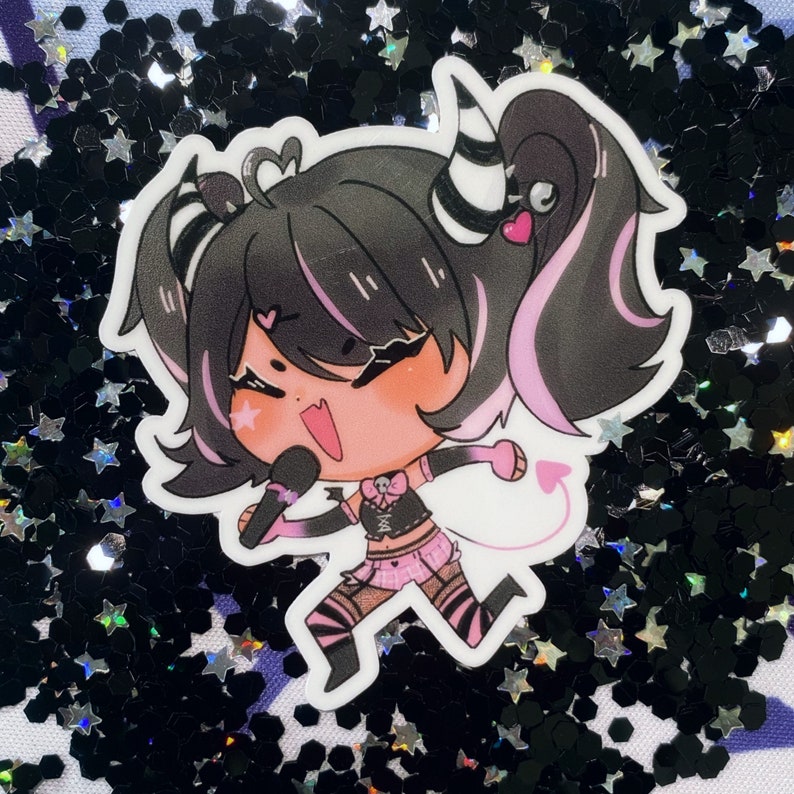 May include: A sticker featuring a cartoon character with black hair, pink highlights, and a black and white striped headband. The character is wearing a black and pink outfit and holding a microphone. The sticker is on a black and silver glitter background.