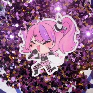 May include: A pink and purple cartoon character with a microphone and a heart on her cheek. She is wearing a black and white outfit with a heart on her chest. The character is on a background of pink and purple glitter.
