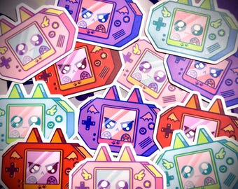 Könnte beinhalten: Eine Sammlung farbenfroher Aufkleber mit einem Cartoon-Design einer Handheld-Spielkonsole. Jeder Aufkleber hat einen Bildschirm, der ein niedliches, wütendes Gesicht mit Pfotenabdrücken zeigt. Die Aufkleber sind in verschiedenen Farben, darunter Rosa, Lila, Rot und Blau.