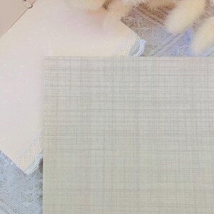 以下が含まれることがあります： 薄いベージュの織り模様の入った質感のある布のクローズアップ。布は滑らかで、柔らかく自然な感触です。