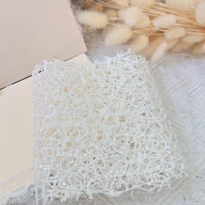 May include: White sparkly mesh fabric with a delicate, intricate pattern. The fabric is soft and lightweight, perfect for crafting or adding a touch of sparkle to any project.
