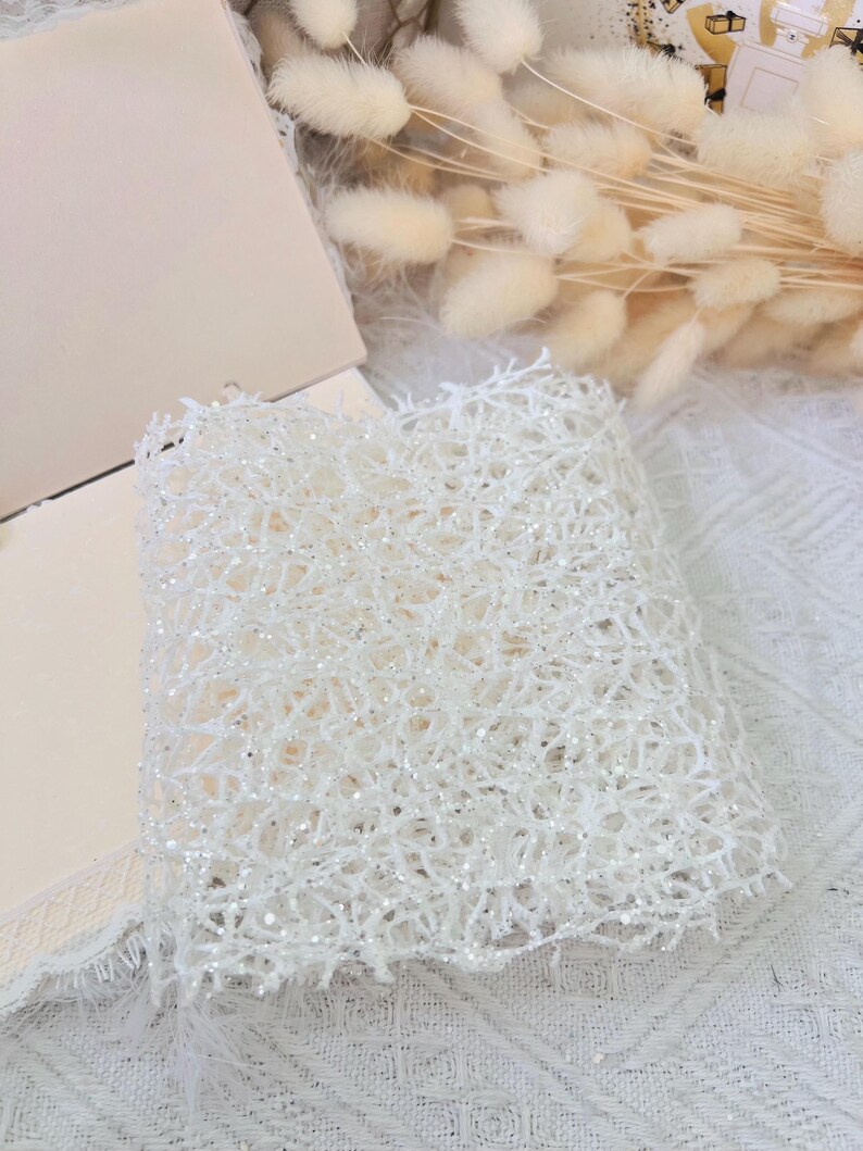 May include: White sparkly mesh fabric with a delicate, intricate pattern. The fabric is soft and lightweight, perfect for crafting or adding a touch of sparkle to any project.