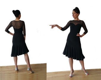 May include: A black dance dress with a sheer neckline and sleeves. The dress has a fitted bodice and a flared skirt with a ruffled hem. The model is wearing silver heels.