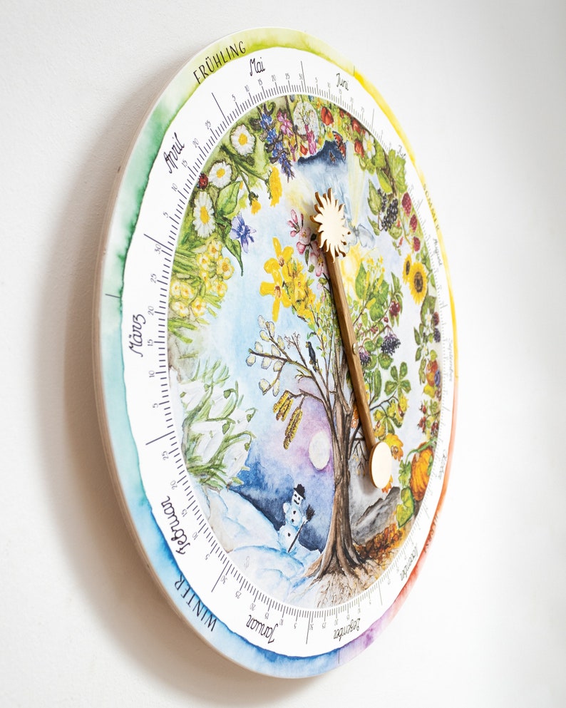 May include: A round, wooden wall clock featuring a watercolor illustration of the four seasons. The clock face displays a tree at the center, surrounded by seasonal imagery and a wooden sun-shaped hand. The clock is mounted on a white wall.