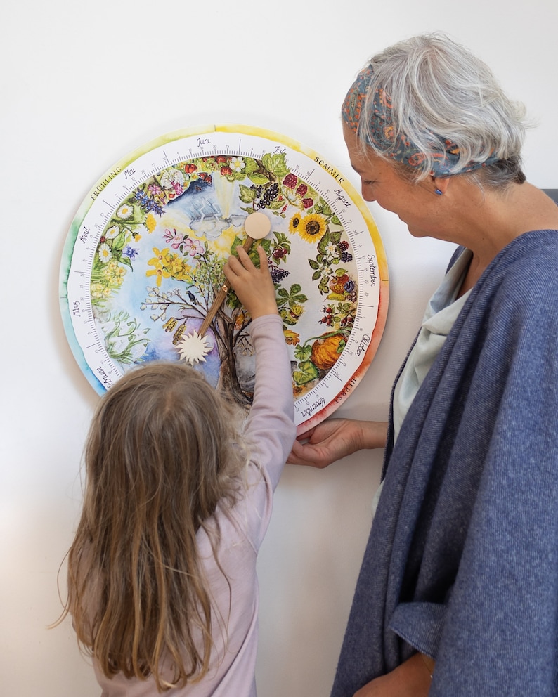May include: A colorful, circular educational calendar featuring illustrations of the seasons. A child and an adult interact with the calendar, pointing to different sections. The calendar is decorated with flowers, fruits, and seasonal imagery.