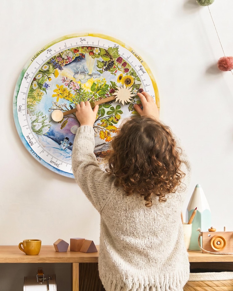 Ein Kind dreht am Zeiger des farbenfrohen, kreisförmigen Jahreszeitenkalenders. Der Kalender zeigt einen fiktiven Jahreszeitenbaum umringt von Blumen, Früchten und saisonalen Elementen. Der Sonnenzeiger zeigt aufs aktuelle Datum, zugleich zeigt er damit an, wie hoch die Sonne zu dieser Jahreszeit über den Himmel zieht.