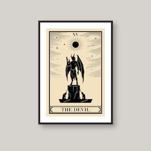 May include: A framed wall art print featuring a black and cream tarot card design titled The Devil. The illustration depicts a horned, winged figure standing on a pedestal above two chained figures, with a sun symbol and stars in the background.