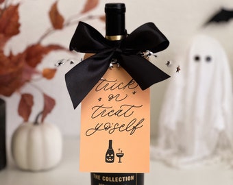 May include: A bottle of red wine with a black bow and a gift tag that says "trick or treat yourself". The tag is orange with a black jack-o'-lantern and wine glass graphic. The bottle is labeled "The Collection Red Wine Blend 2020 California."