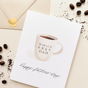 May include: White card with a hand-drawn illustration of a coffee mug with the text "World's Best Dad" and the words "Happy Father's Day" written in cursive.