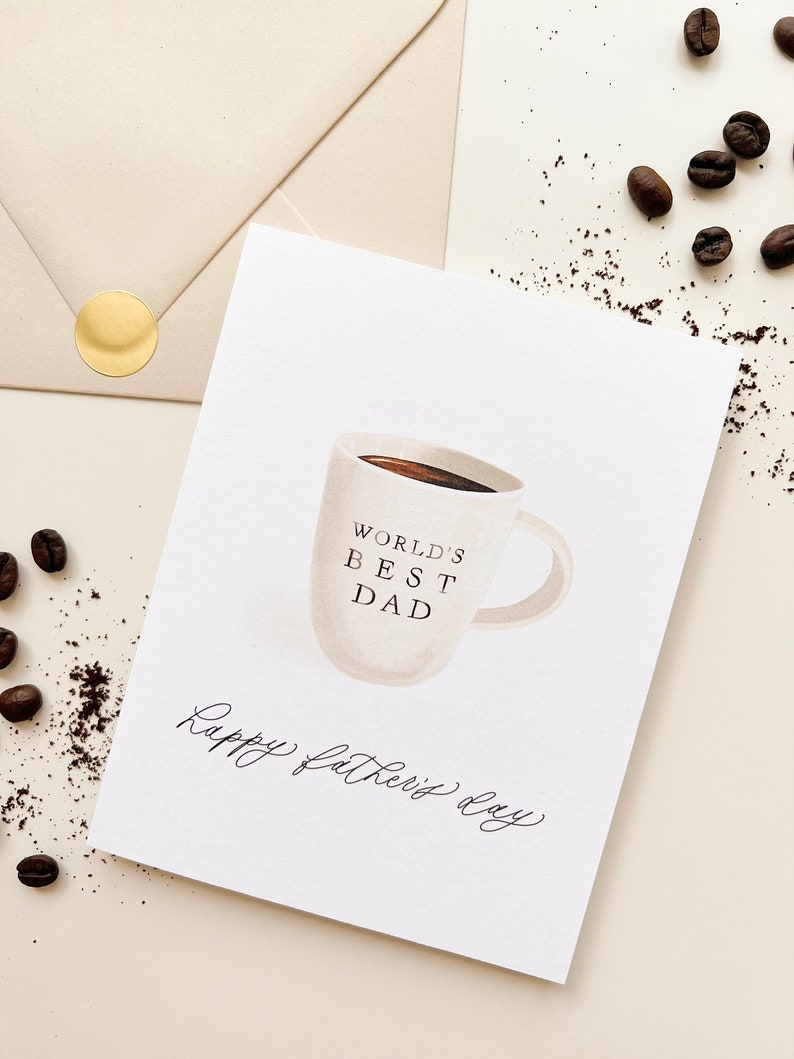 May include: White card with a hand-drawn illustration of a coffee mug with the text "World's Best Dad" and the words "Happy Father's Day" written in cursive.