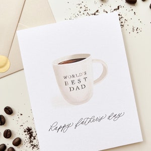 May include: A white card with a coffee cup illustration and the text "World's Best Dad" on the cup. The card also has the text "Happy Father's Day" written in cursive.