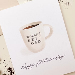 May include: A white card with a brown coffee mug illustration. The mug says "World's Best Dad" and the card says "Happy Father's Day" in cursive.