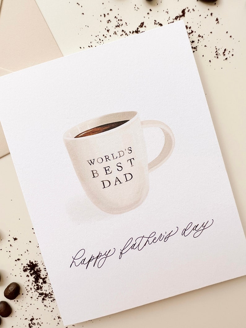 May include: A white card with a brown coffee mug illustration. The mug says "World's Best Dad" and the card says "Happy Father's Day" in cursive.