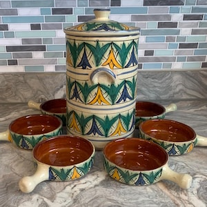 May include: A ceramic canister with a lid and four matching small bowls, all featuring a hand-painted pattern of green, yellow, and blue leaf-like shapes on a cream background. Each bowl has a single handle and a smooth, solid brown interior.