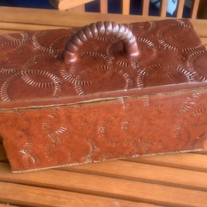 May include: A rectangular terracotta-colored ceramic box with a matching lid and a curved handle. The entire exterior surface, including the lid, features a repeating embossed pattern of small, semi-circular, dash-like impressions.