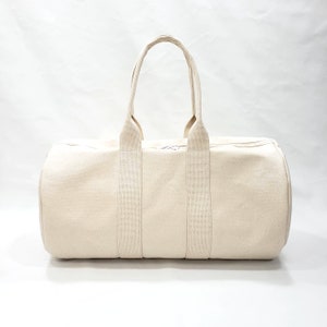 May include: A cream-colored canvas duffel bag with two long straps and a zipper closure.
